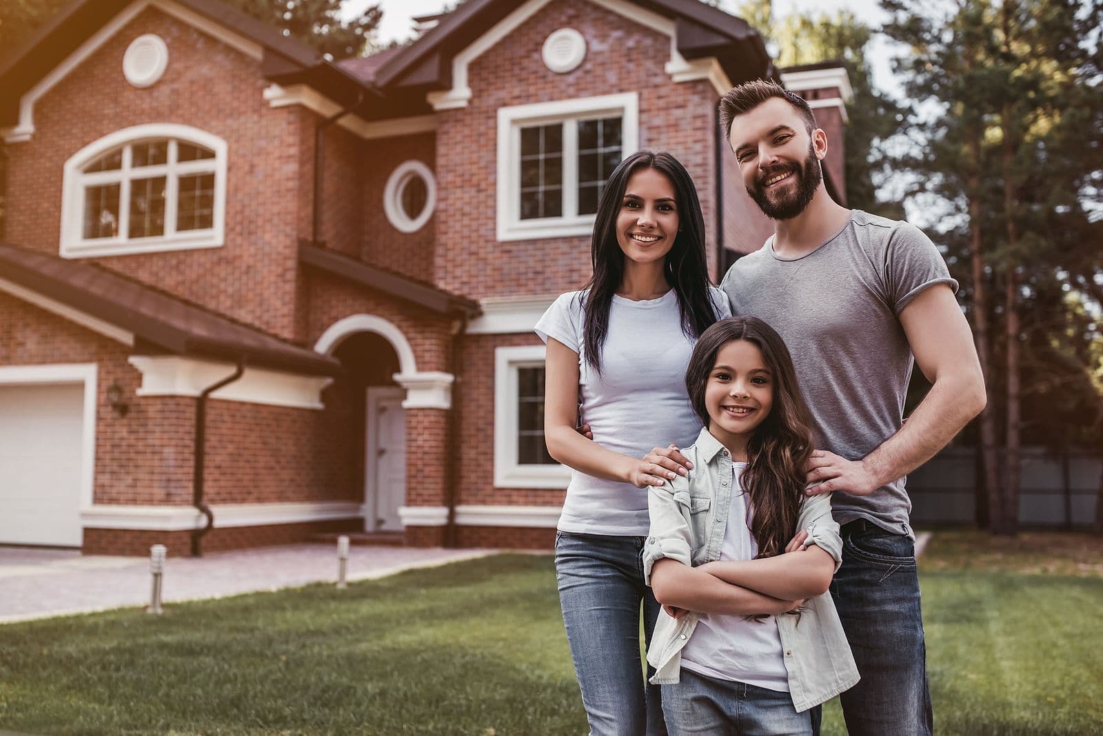 A family smiles together in front of a red brick house.