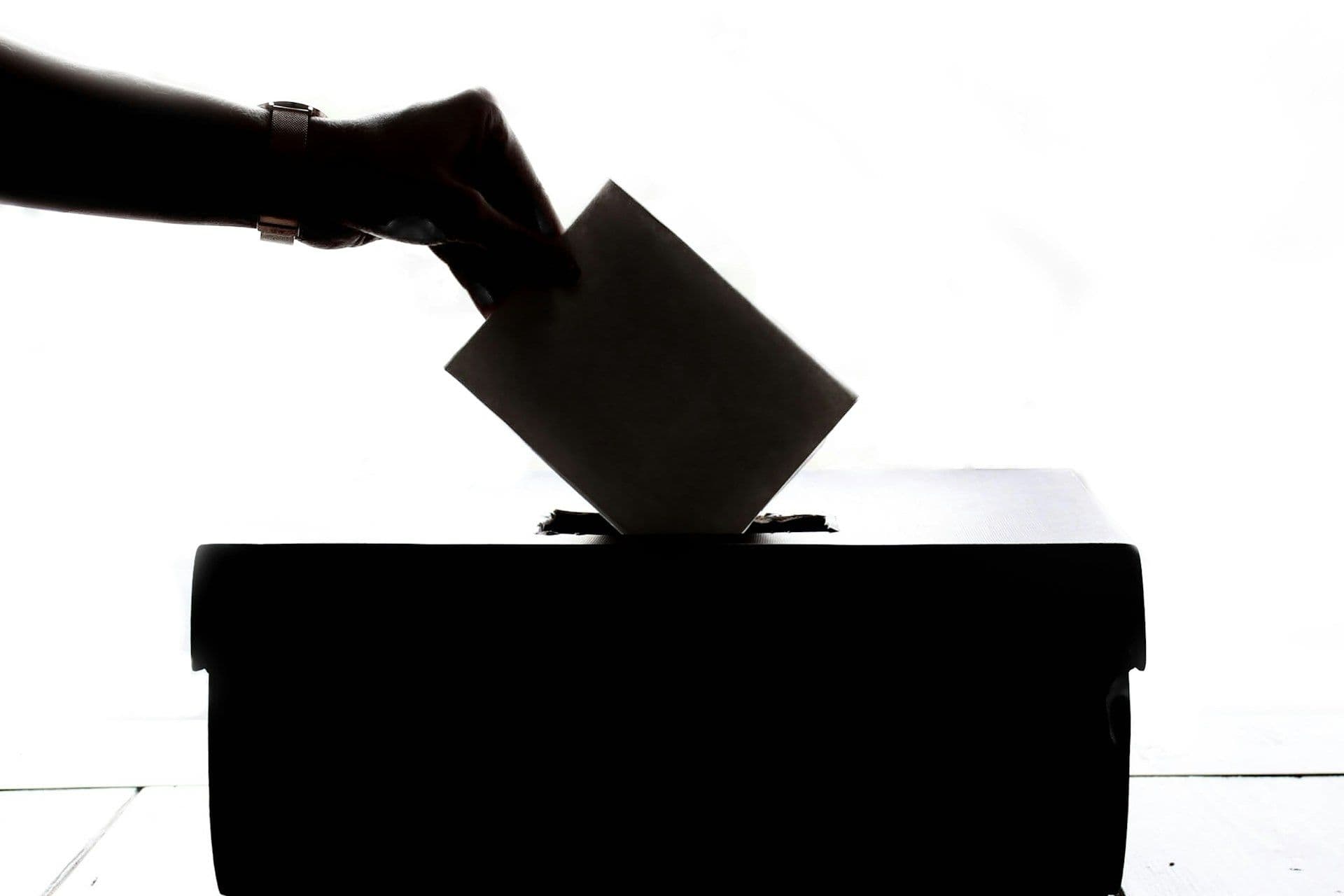 The silhouette of a person dropping a vote into a box.